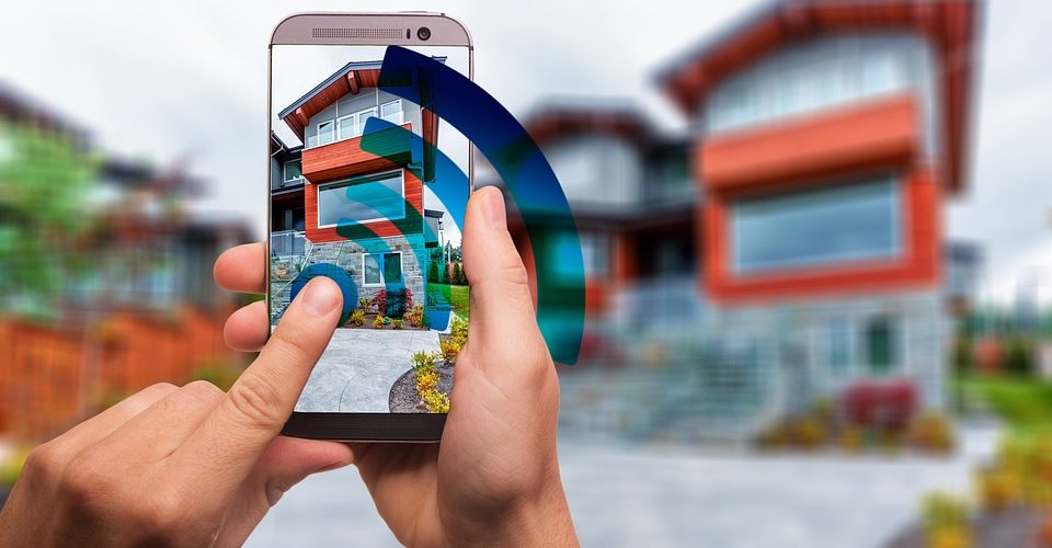 Smartphone auf dem App geöffnet ist, großes Wlan-Symbol im Vordergrund, im Hintergrund ein Haus